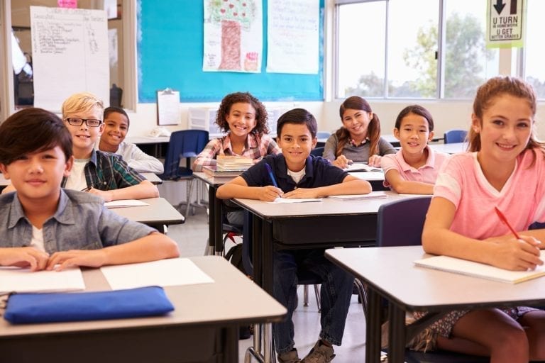 Smiling elementary school kids sitting at desks in classroom