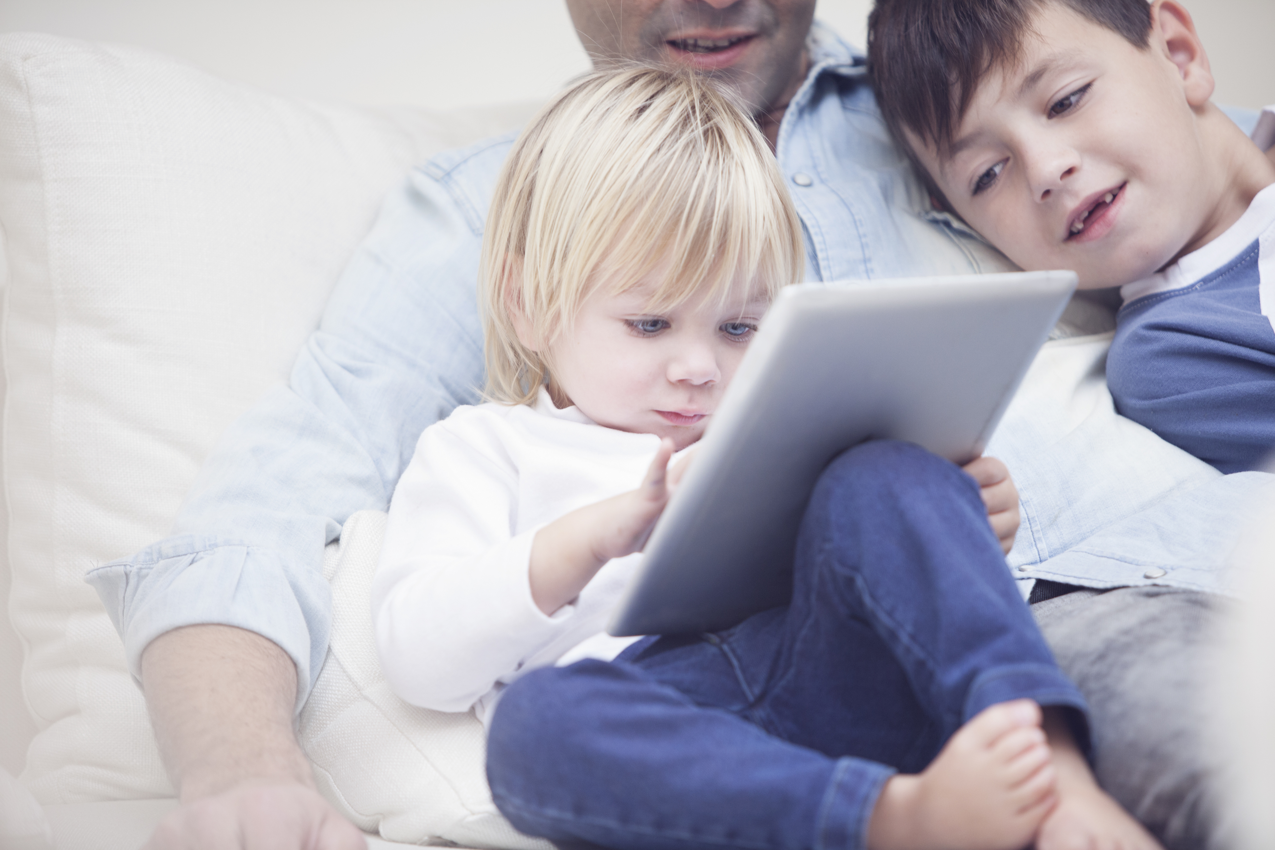 young boy watches an iPad with his brother while sitting on his father's lap