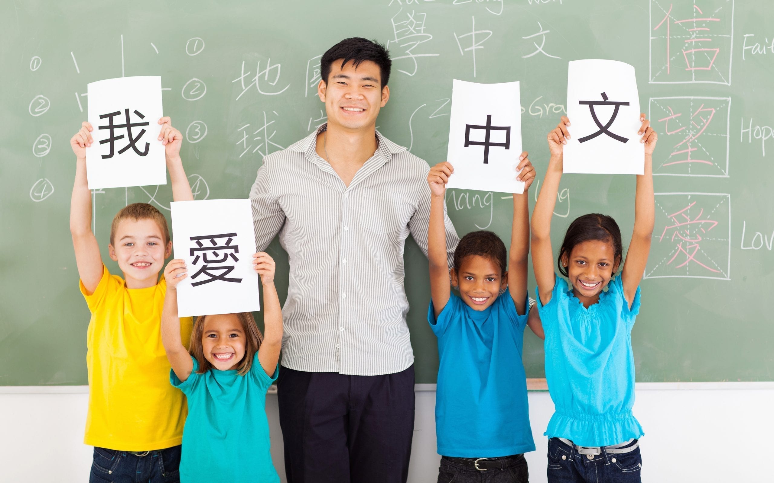 friendly male chinese teacher with group multiracial primary students holding papers saying i love chinese