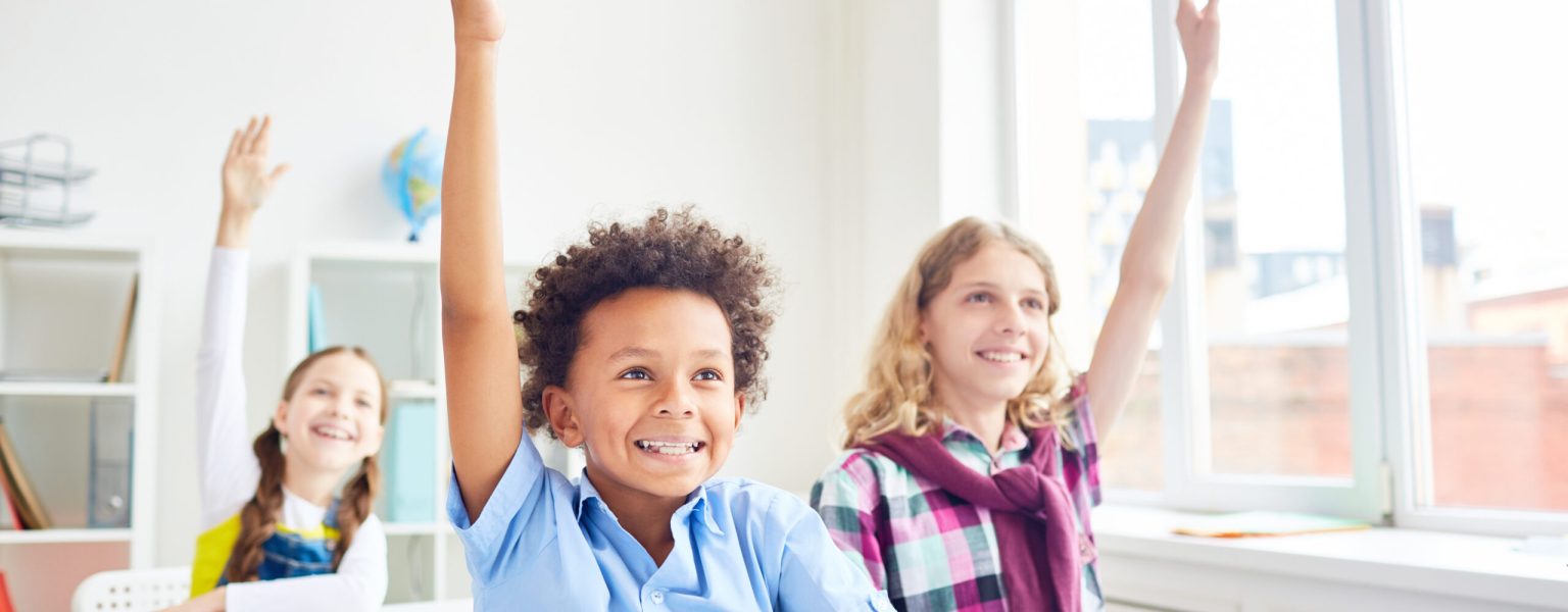 Kids raising hands Happy and clever learners of elementary school raising their hands at lesson